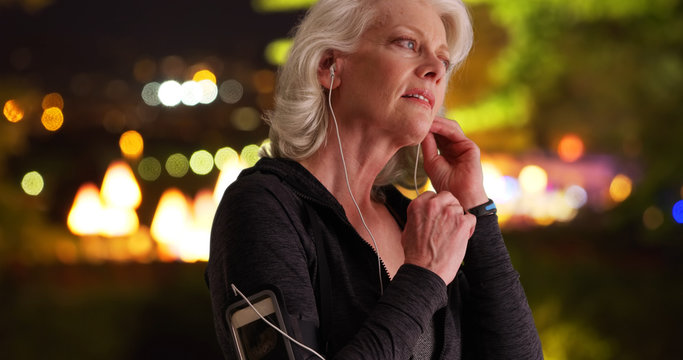 Active senior woman puts in earbuds and checks fitness tracker on night run