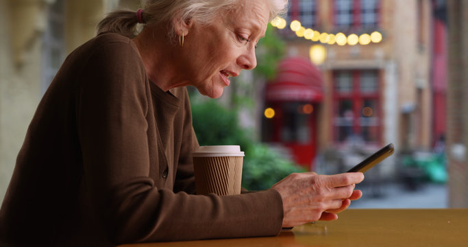 Worried older Caucasian woman on cafe patio texting with friend on cellphone