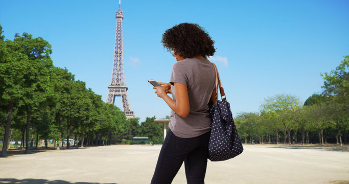 Rear view of black woman tourist sending text message in front of Eiffel tower