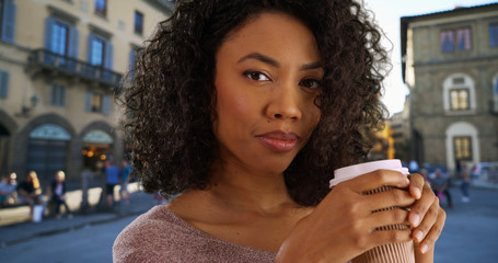 Happy young black woman drinking coffee in town square out of paper to go cup