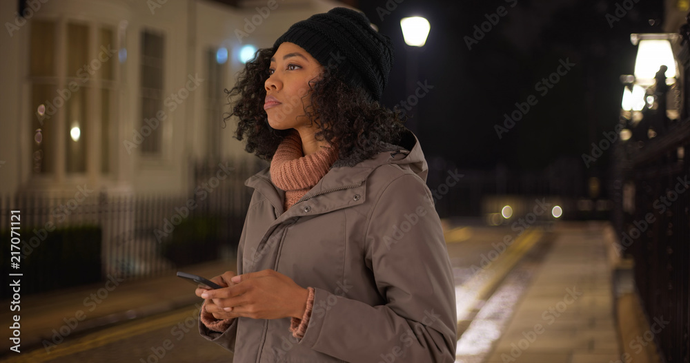 Wall mural Black woman removing gloves to use smartphone rideshare app to call for a ride - Wall murals