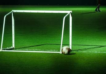 Soccer ball and goalpost on green soccer pitch at night