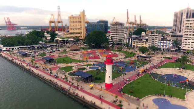 Aerial: Small city by the ocean. Small dock with playing ground and lighthouse (miniature look)