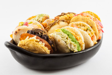 Arepas with assorted fillings served in a black ceramic dish on white background
