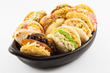 Arepas with assorted fillings served in a black ceramic dish on white background