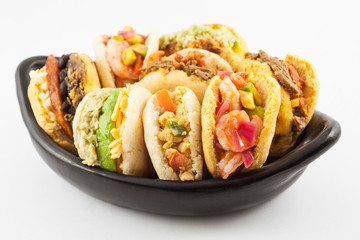 Arepas with assorted fillings served in a black ceramic dish on white background