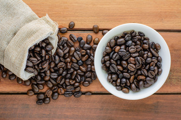 Roasted dark coffee beans  in sack and bowl on wooden background.Top view.