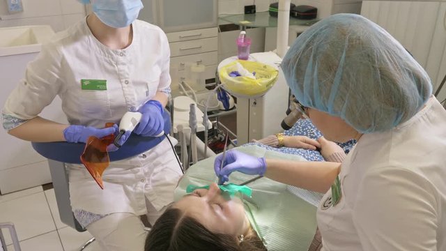 Woman at dentist clinic gets dental treatment to fill a cavity in a tooth. Dental restoration and composite material polymerization with UV light and laser. The doctor works with an assistant.