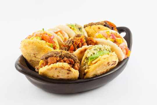 Arepas with assorted fillings served in a black ceramic dish on white background