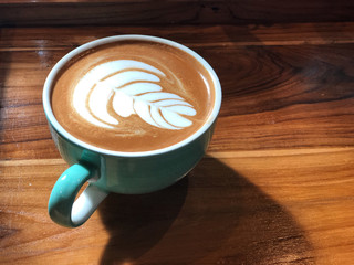 Heart latte art coffee in green and white cup on the vintage wooden table with natural light .Wake up and full fill energy, top view and copy space
