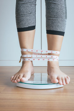 Woman foot standing on electronic weigh scales with tape measure legs winded