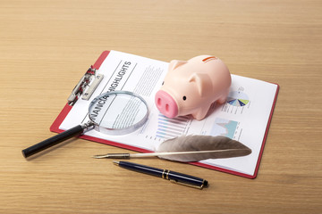 pig coin bank with clipboard, magnifier, feather pen on the wood table
