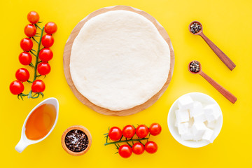 Ingredients for cooking vegetarian pizza. Rolled pizza dough, cherry tomatoes, olive oil, cheese mozzarella, spices on yellow background top view mockup