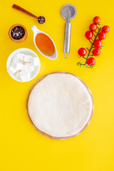 Make pizza concept. Pizza dough and ingredients for filling. Cherry tomatoes, olive oil, cheese mozzarella, spices near knife for pizza on yellow background top view mockup copy space