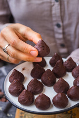 Woman hands holds chocolate truffle confectionary made with grated chocolate, cocoa or carob powder, coconut oil, chopped nuts, sweet nuts. Healthy vegan sweets or vegetarian sweets.