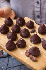 Woman hands holds chocolate truffle confectionary made with grated chocolate, cocoa or carob powder, coconut oil, chopped nuts, sweet nuts. Healthy vegan sweets or vegetarian sweets.