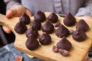 Woman hands holds chocolate truffle confectionary made with grated chocolate, cocoa or carob powder, coconut oil, chopped nuts, sweet nuts. Healthy vegan sweets or vegetarian sweets.