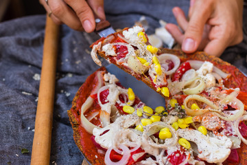 Woman hands hold a piece of raw vegan pizza with dehydrated dough, raw tomato sauce, vegan mayonnaise, corn and fresh vegetables. Healthy Italian food