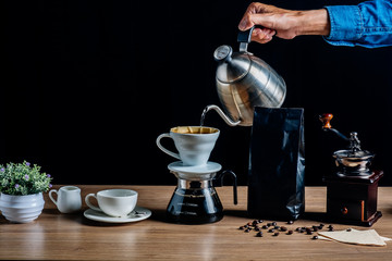 Drip brewing coffee concept.Barista pouring hot water on roasted coffee ground with filter on black background.