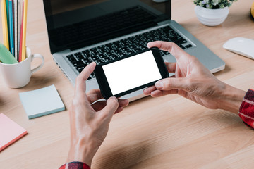 Smart phone mock up concept.Hipster man hand holding blank screen smart phone on desk table with office supplies.