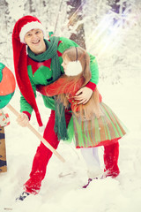 father and little daughter walk in costumes of flowers traditional for elves Santa's helpers in the winter forest under the snow with a chest of gifts and giant candy new year