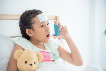 Young asian girl sitting on bed and using broncodilator inhaler for relieve asthma symptom