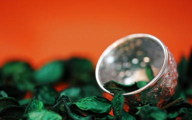 Dried green tree petals decoration and silver bowl closeup orange texture blur background
