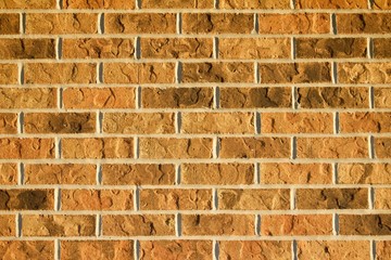Textured brick wall background in varying colors of brown and tan illuminated by filtered low setting sun