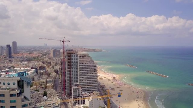 Aerial footage of Tel Aviv's skyline along the coastline with people at the beach on a summer's day