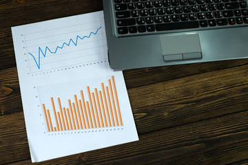 Notebook laptop computer and financial graph on white paper on working table, business planning vision and finance analysis concept.