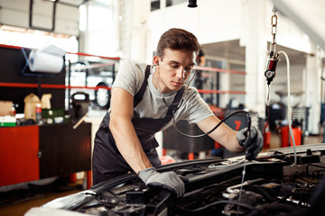 Fototapeta na wymiar A young man is busy with checking an automobile engine: car repair and maintenance