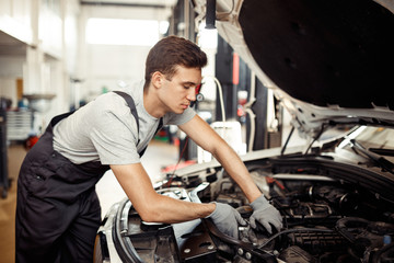 Naklejka na ściany i meble Car service and maintenance: an automechanic is repairing a vehicle