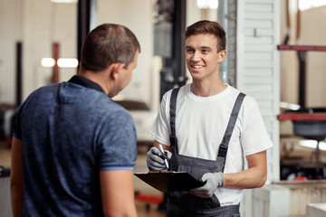 An attractive automechanic is smiling to his client during their appointment