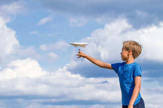 Boy throwing paper plane against blue sky