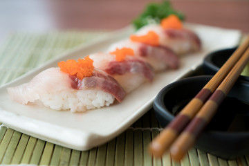 Hamachi sushi on white plate along with Japanese sauce and green leaf decoration, Japanese food, close up at sushi ..