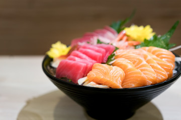Mixed sliced fish sashimi on ice in black bowl. Sashimi Salmon Tuna Hamachi Prawn and Surf Calm set, raw fish, japanese food in Asian restuarant.