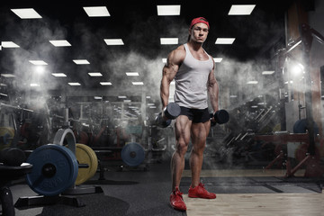 Fototapeta na wymiar Athletic muscular bodybuilder with dumbbells in gym