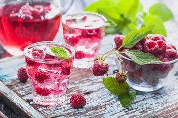 Red raspberries cocktail with ice and fresh mint on a old wooden table