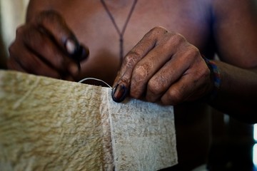 ticuna indian tribal member stitching a tree bark artifact together