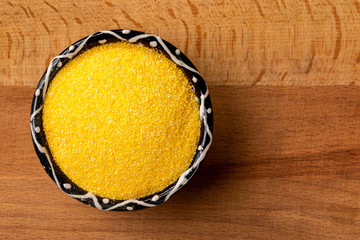 Obraz na płótnie Canvas Closeup top view bowl of raw polenta cornmeal at left corner of wooden background.