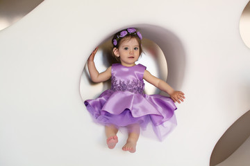  Little girl in a white room with flowers and in a gray dress. The baby is smiling. The girl gives flowers. Elegant dress dressed on a child