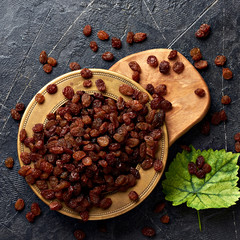 Heap of brown raisins on plate. Top view of dried grapes with green leaf.