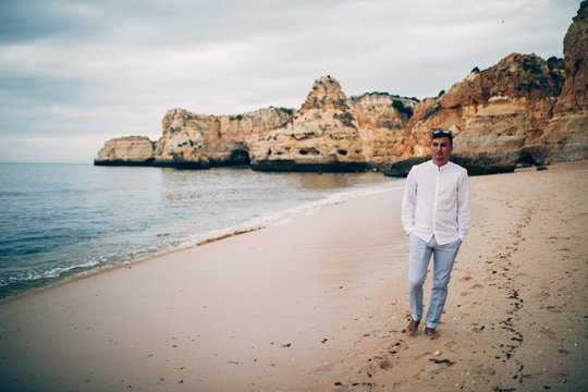 Young Happy Man Walking In J A White Shirt On The Beach And The Sea At Sunset