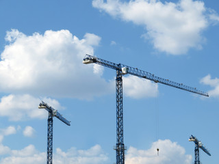 Construction cranes on cloudy blue sky background