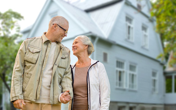 old age, accommodation and real estate concept - happy senior couple holding hands over living house background