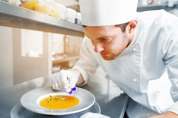 food cooking, profession and people concept - happy male chef cook serving and decorating plate of...
