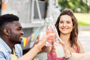 celebration, leisure and people concept - happy friends clinking bottles with non alcoholic drinks at food truck