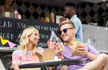 leisure, celebration and people concept - happy friends clinking bottles of non-alcoholic drinks and eating wok at food truck