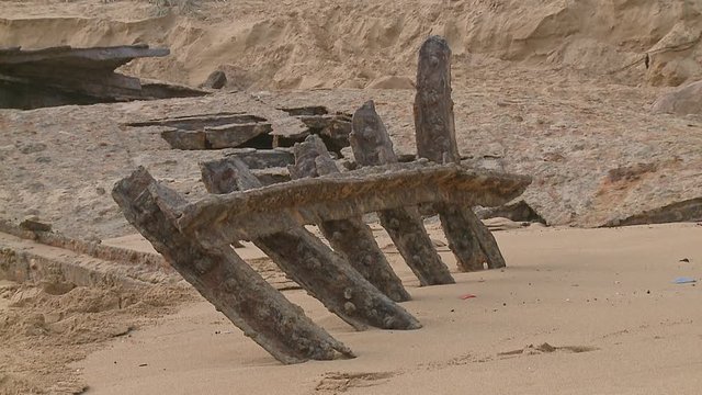 Old, rusty ribs from the hull of a stranded ship in front of other pieces of debris on a sandy beach