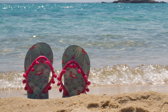 Colorful beach flip flops in a sand near the sea. Woman slippers with pink flamingos. Summer lifestyle. Vacation and travel concept.